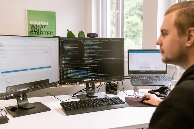 Entwickler arbeitet an mehreren Monitoren mit Code und Dokumenten