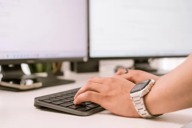 Hände an Tastatur und Maus vor zwei Monitoren