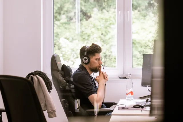 Entwickler mit Kopfhörern im Support-Call am Fenster